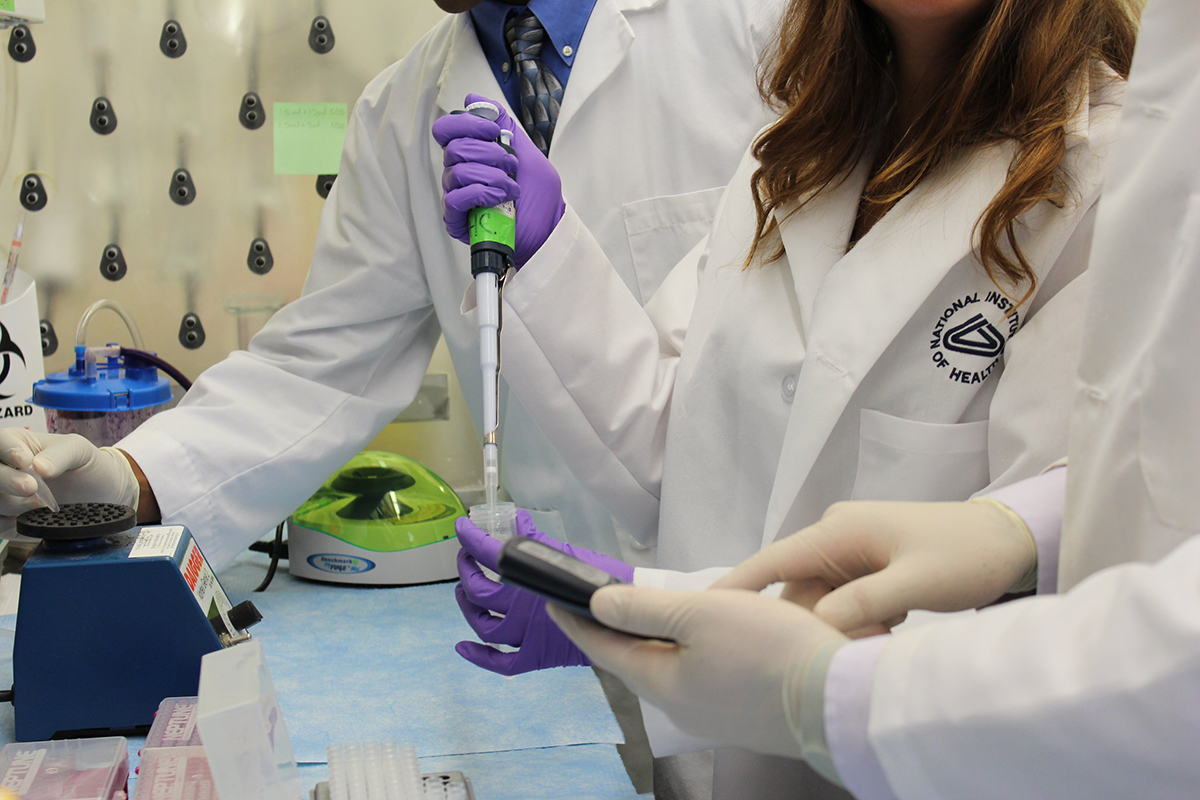 Three scientists holding pipettes and equipment conducting research at the NIH Clinical Center