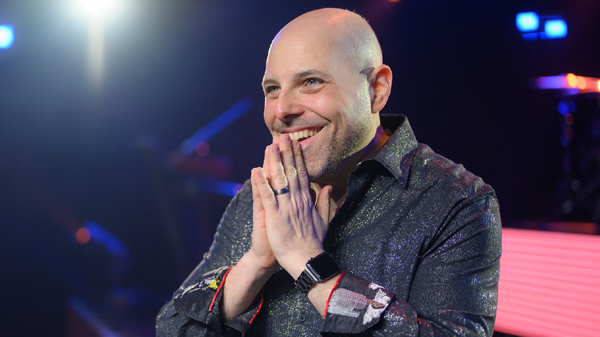 Cancer survivor stands on a stage with hands clasped together and a smile on his face.