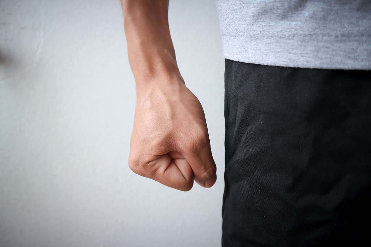 Fist of angry man wearing a gray shirt and black pants who is experiencing blood vessel strain