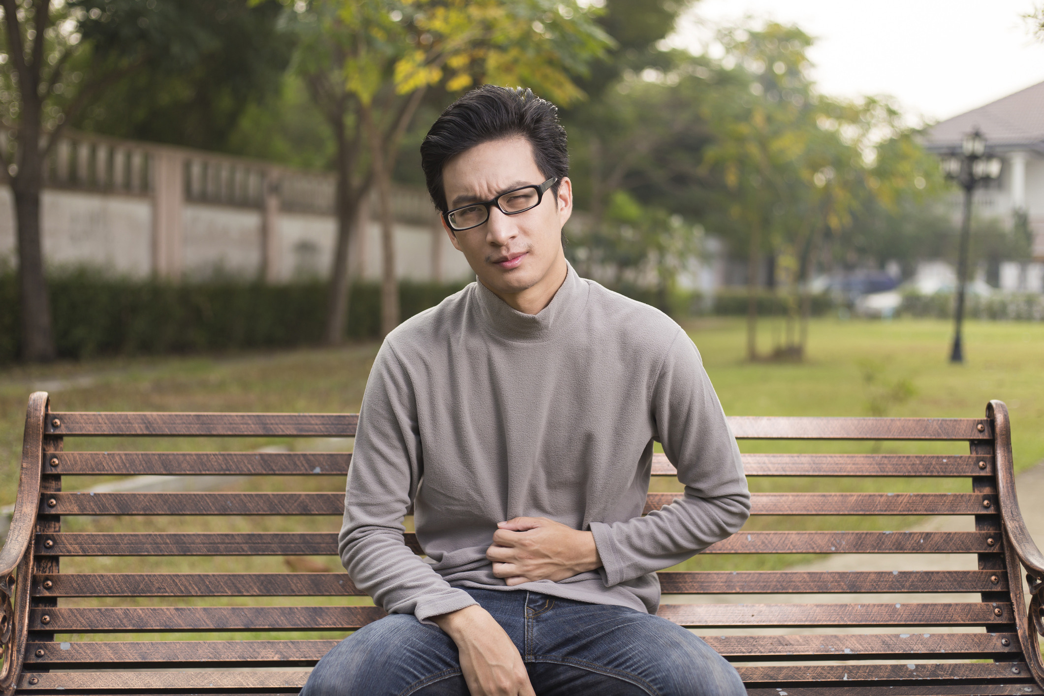 Man on park bench holding his stomach in discomfort