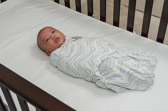 Swaddled baby lying on its back in a crib