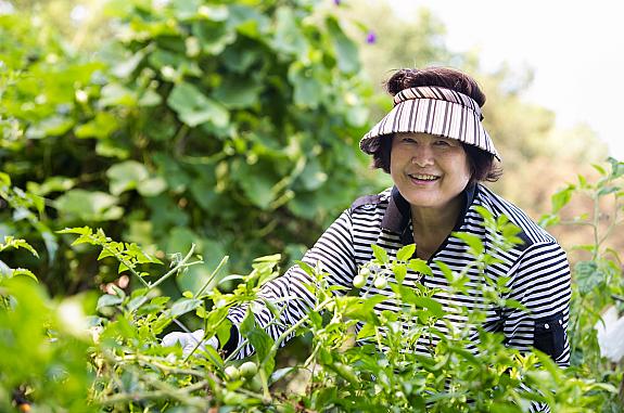 A woman is standing in a garden and smiling at the camera.