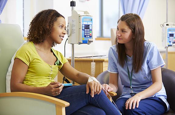 Female patient and female nurse sit looking at each other while the patient has an IV in her hand.