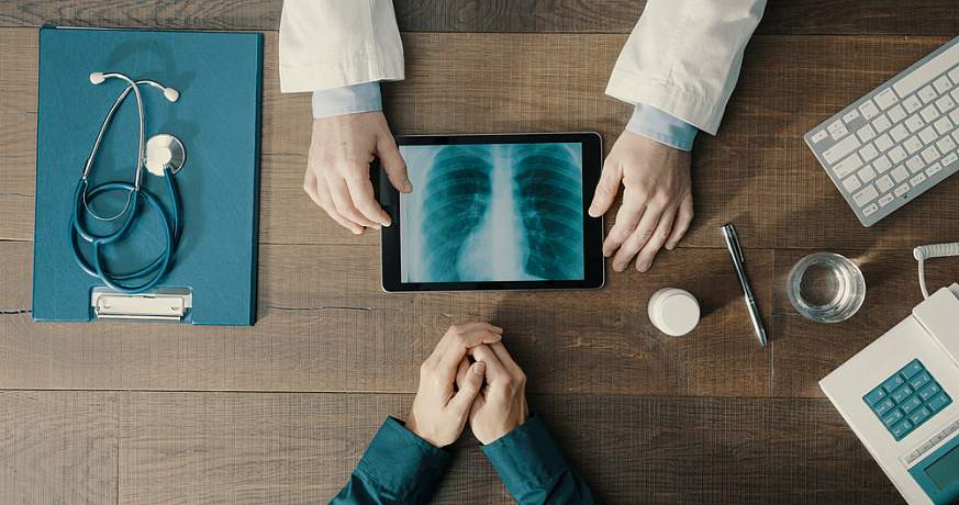 Doctor meeting a patient in the office and giving a medical consultation, he is using a digital tablet and checking medical records