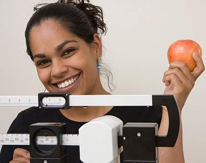 Photo of a young woman standing on a scale, holding an apple