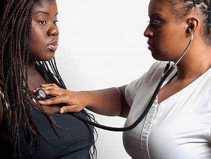 Doctor using a stethoscope to examine an overweight African-American woman.