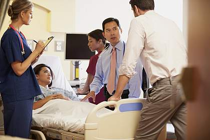 Medical team meeting around female patient in hospital room.