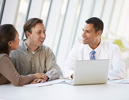 Doctor using laptop and consulting with young couple.