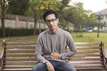 Man on park bench holding his stomach in discomfort