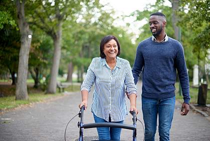 Mature woman using a walker while a young man assists her in the park Mature woman using a walker while a young man assists her in the park