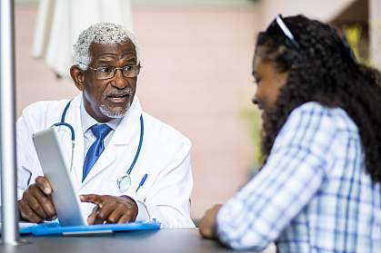 A senior black doctor explaining something on a tablet to a young black womanA senior black doctor explaining something on a tablet to a young black woman