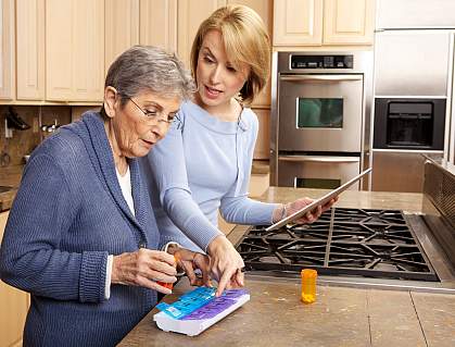 Young woman helping senior in kitchen to sort her medications Young woman helping senior in kitchen to sort her medications