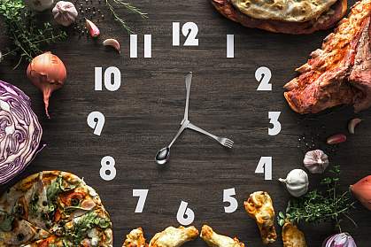 Black wooden clock with utensils as hands and surrounded by food