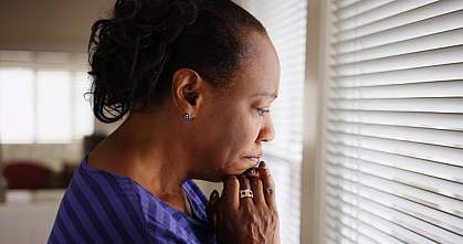 An older black woman mournfully looks out a window. An older black woman mournfully looks out a window.