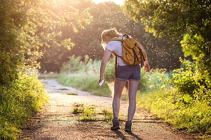 Woman on a hike in the forest applying insect repellent as mosquitoes swarm around her.