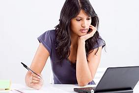 Close-up of a woman with a laptop and a writing pad.