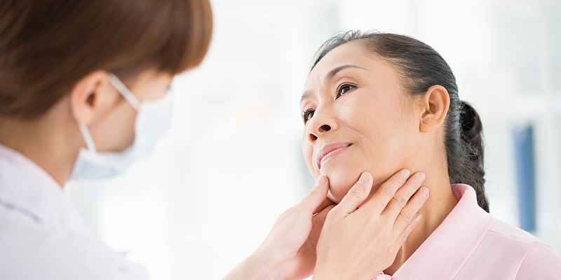 A doctor examining a patient's thyroid in the neck area.
