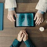 Doctor meeting a patient in the office and giving a medical consultation, he is using a digital tablet and checking medical records