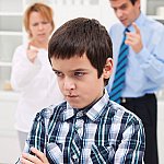 An indignant boy with his arms folded and back turned toward his parents, who are lecturing him.