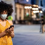 Black women with protective face mask using a smart phone on the street