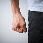 Fist of angry man wearing a gray shirt and black pants who is experiencing blood vessel strain