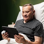 A man in a hospital bed looking at a computer tablet