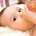 Infant watching someone while drinking from a bottle.