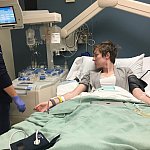 A medical technician watches the monitor of a woman with IVs in a hospital bed.