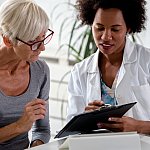 Female doctor speaking with an elderly female patient while looking at test results.