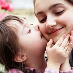 Child with Down Syndrome kissing the cheek of an adult.
